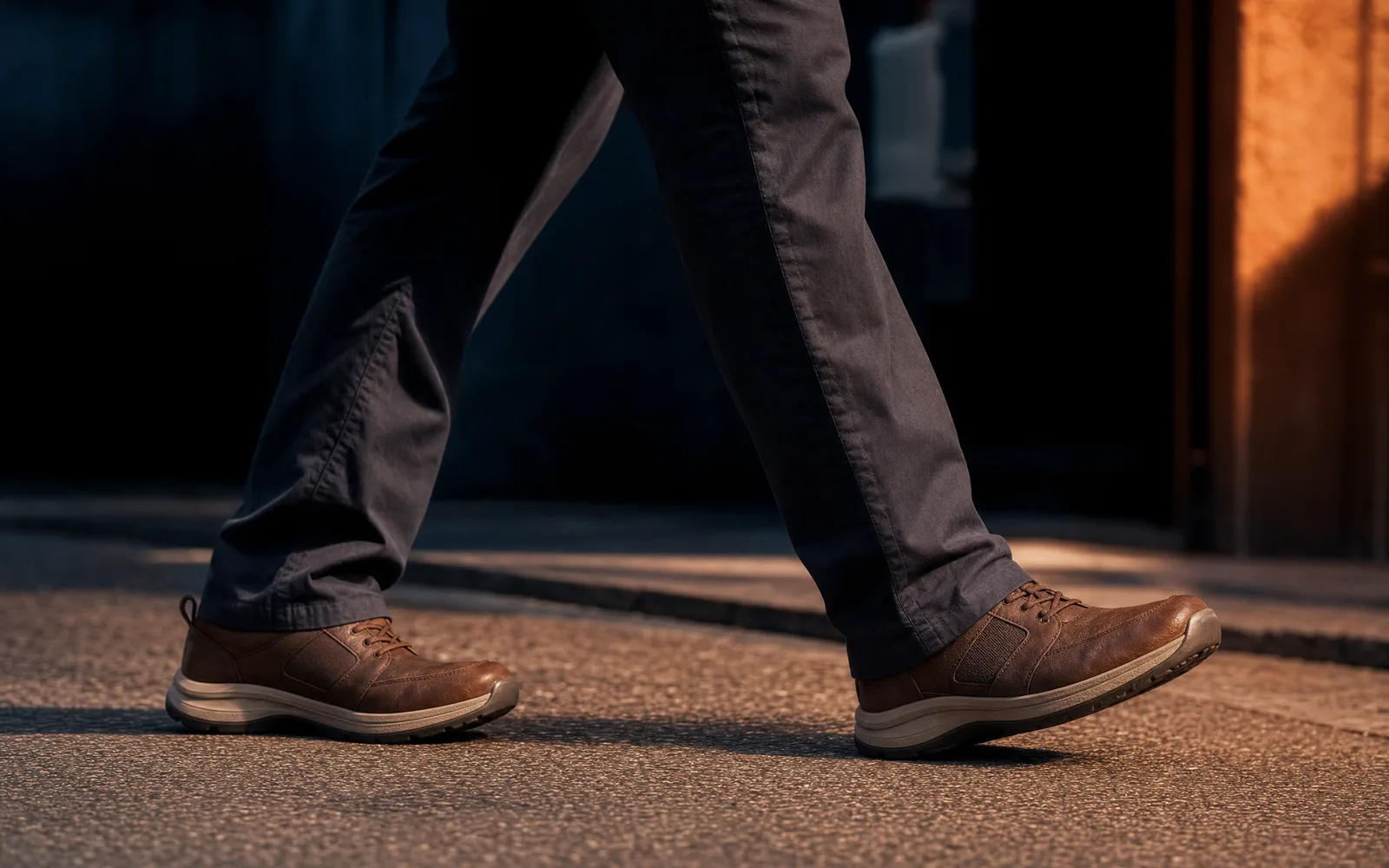 Chaussures orthopédiques homme portées lors d’une marche active en extérieur, ambiance sombre et lumière terracotta