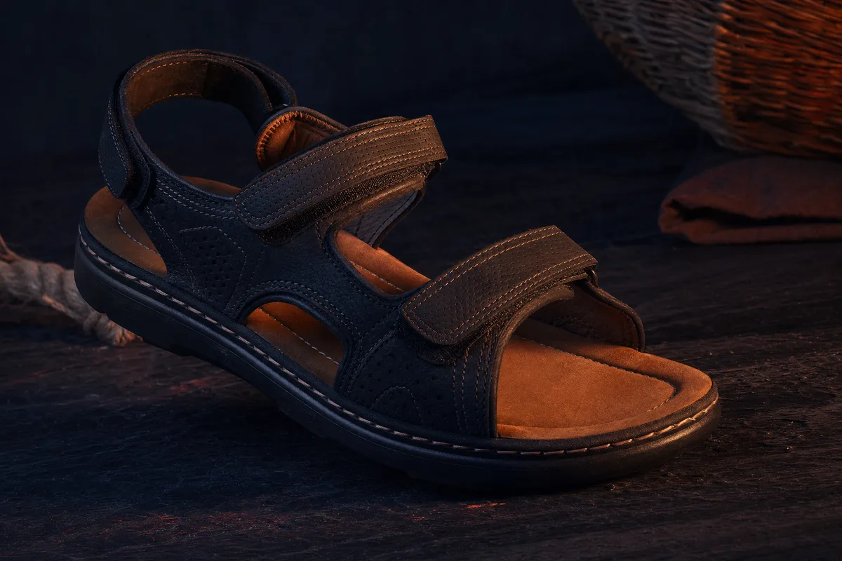 Chaussures orthopédiques homme, sandale réglable présentée sur fond sombre avec accent terracotta